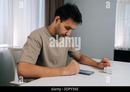 Focused man connecting smart home device using smartphone, looking at application settings, setting up and controlling smart socket from mobile app Stock Photo