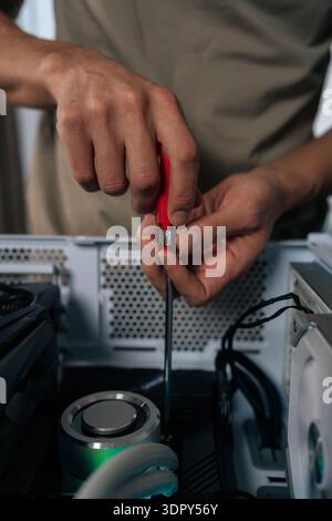 Technician hands maintaining and upgrading a personal computer, assembling internal hardware components with screwdriver, performing service and Stock Photo