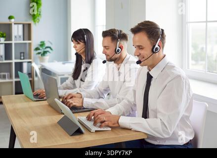 Support agents with headsets working on laptops in a bright modern office Stock Photo