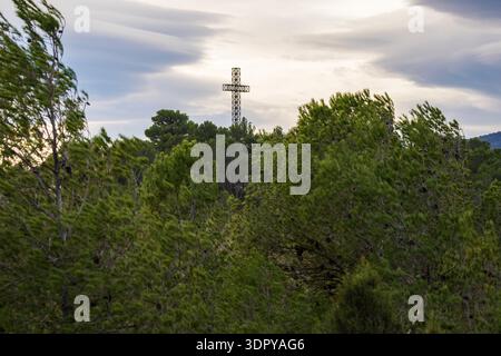 Iron cross on the summit of San Cristobal with motion blur caused by wind in the foreground pine trees, Alcoy, Spain Stock Photo