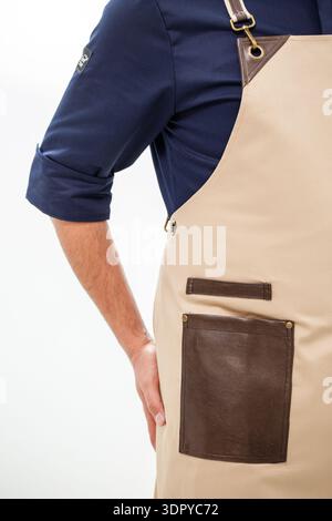 Premium beige canvas chef apron featuring brown leather pocket, reinforced leather accents, adjustable suspenders, and brass hardware Stock Photo
