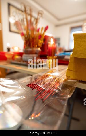 Chinese New Year altar with incense sticks, lit candles, red decorations, and ceremonial items on table in home setting Stock Photo
