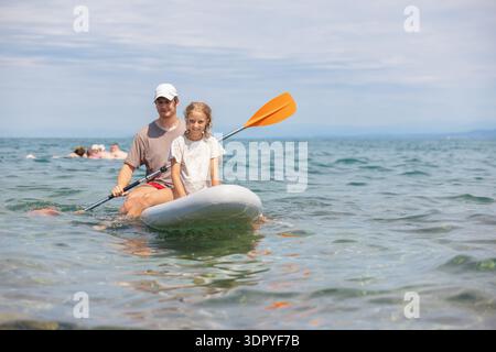 Brother and sister enjoy paddleboarding together on a sunny summer day at the sea, experiencing fun and active family time. Stock Photo