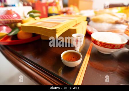 Vietnamese Lunar New Year altar with incense sticks, tea cup, rice bowl, and ceremonial offerings on wooden table Stock Photo