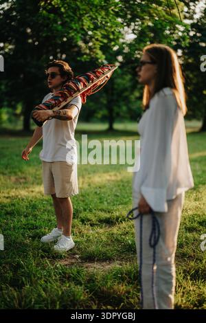Man with colorful kite in the park with a friend enjoying a sunny outdoor moment Stock Photo