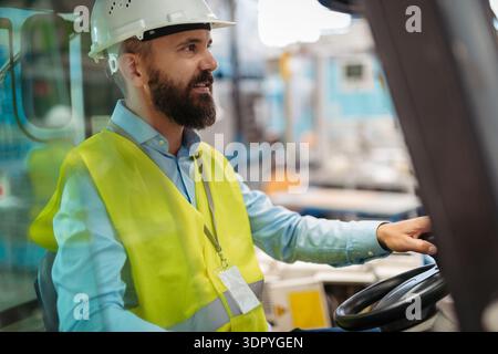 Male factory supervisor driving foklift in industrial production hall. Stock Photo