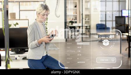 Scrolling smartphone, woman wearing blazer sitting on desk edge at office with AR checkout HUD, mug Stock Photo