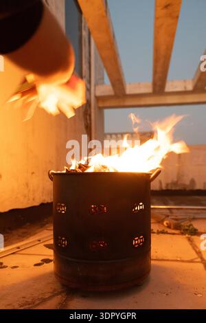 Burning wood in metal fire pit on rooftop at dusk with wooden beams and warm glow Stock Photo
