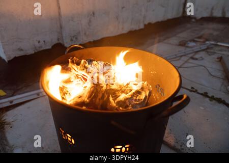 Burning wood logs in metal fire pit outdoors at night with glowing embers and warm flames Stock Photo
