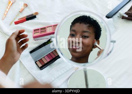Round tabletop mirror is reflecting while makeup brushes and palettes are resting on towel at bed Stock Photo