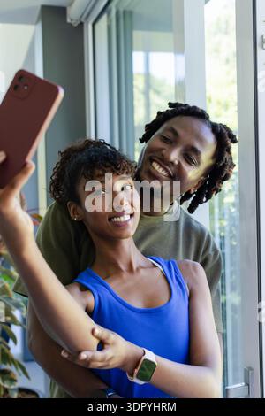 African-American couple posing by door woman in blue top with watch holding rose phone man hugging Stock Photo