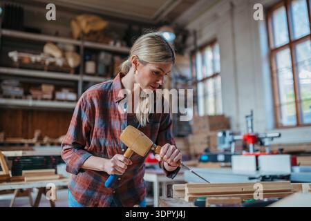 Female carpenter working on her product in carpentry workshop. Female carpenter working on her product in carpentry workshop. Small business concept. Stock Photo