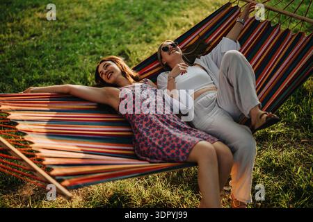 Two friends relax in a colorful hammock outdoors on a sunny summer day Stock Photo