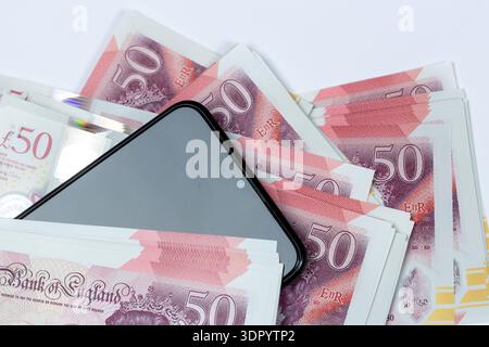A close up of a stack of Fifty Pound Notes on top of a mobile phone. Stock Photo