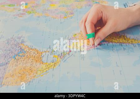 Person Marks a Location on a World Map Using a Pen and a Green Tool Stock Photo