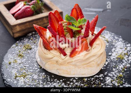 Strawberry Pavlova Dessert With Fresh Fruit and Mint Served on a Dark Plate Stock Photo