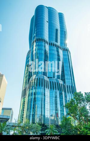 Modern glass skyscraper with curved facade and green trees in Hong Kong city, China. Green city, modern business district, corporate architecture Stock Photo