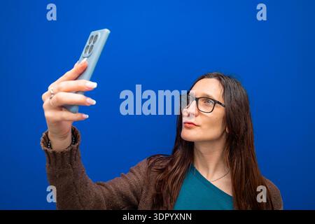 Woman holding smartphone, taking selfie. Wearing eyeglasses, capturing digital content for social media and online communication Stock Photo