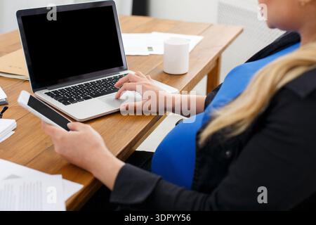 Pregnant Woman Using Laptop and Smartphone at Home Office on a Wooden Table Stock Photo