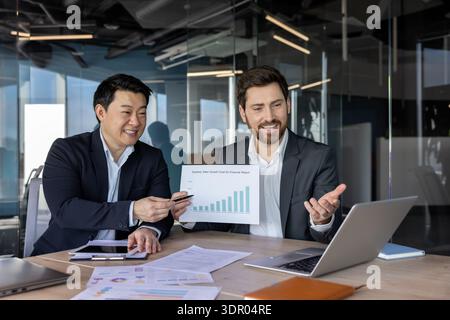 Businessmen analyzing sales growth chart, collaborating on a financial report during an online video conference, discussing data, and planning strategy in a modern office meeting Stock Photo