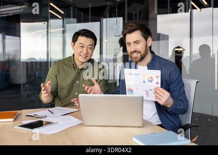 Diverse business professionals in a modern office conducting an online video conference, discussing financial charts and collaborating during a remote workplace meeting Stock Photo