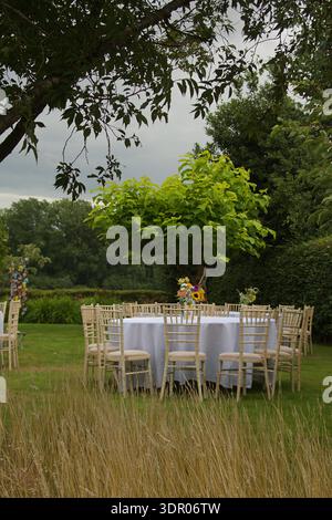 Table in a garden ready for a reception party with chairs and flowers Stock Photo