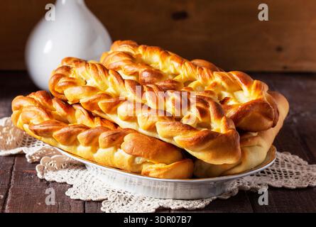 Braided buns with cottage cheese filling, served with tea. Yeast-based pastries, a cup of black tea, and cotton flowers on a wooden table. Rustic styl Stock Photo