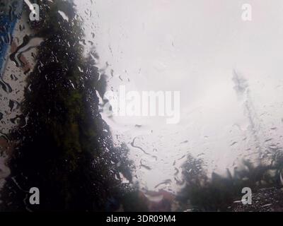 Close up of raindrops on a window pane with a bluerred outdoor background of trees and cloudy grey sky. Stock Photo