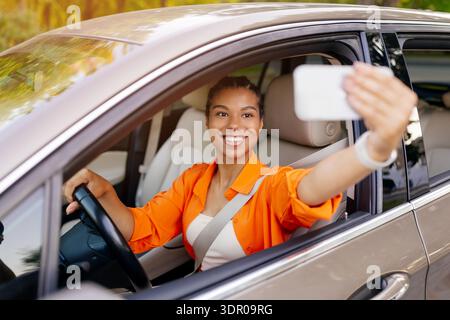 Young black woman taking selfie inside car while driving, capturing joyful moment Stock Photo