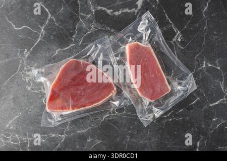Frozen tuna fish steak in transparent plastic package on dark grey marble background. Healthy sea food. Stock Photo