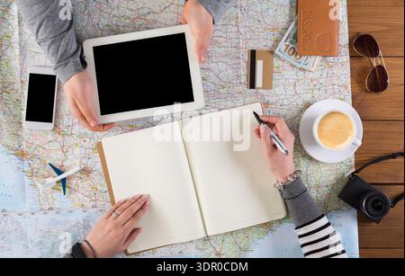 Planning a Trip With a Tablet, Map, and Notebook on a Wooden Table in a Casual Setting Stock Photo