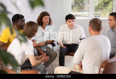 Cheerful male colleagues friendly talking sitting in circle on chairs Stock Photo