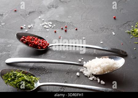 Various Spices and Herbs on Metal Spoons Placed on a Dark Surface in a Kitchen Setting Stock Photo