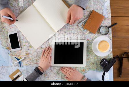 Group Planning a Trip Using Map, Tablets, and Notes at a Wooden Table With Coffee Stock Photo