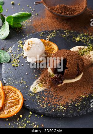 Dessert Served on a Dark Plate With Chocolate, Ice Cream, and Orange Slices in a Kitchen Setting Stock Photo