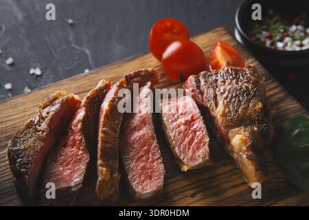 Cooked Beef Steak Served on Wooden Board With Cherry Tomatoes and Spices for Seasoning Stock Photo