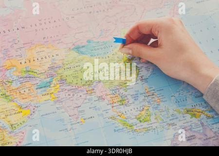 Hand Marks Location on a Map of Asia With a Blue Arrow Pointing to China for Travel Planning Stock Photo