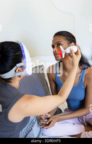 Red-light therapy device is emitting glow on couch near white LED mask and pillow Stock Photo