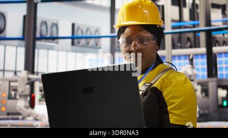 Solar panels plant technician uses laptop to oversee systems, ensuring machinery operates at optimal efficiency. Photovoltaics plant employee uses software on notebook to maintain operations, camera A Stock Photo