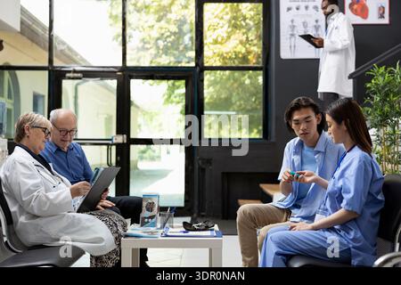 Female nurse doing routine blood glucose test on patient in clinic waiting room before medical appointment. Hospital staff uses digital glucometer to measure blood sugar levels accurately. Stock Photo