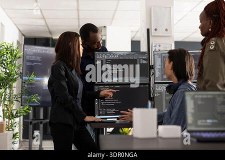 Professional programmers collaborate in tech workspace, analyzing coding scripts on computer monitors. Diverse male and female developers discussing app development and website solutions. Stock Photo