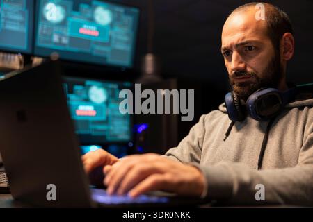 Bearded programmer writing code and developing software for cloud computing and secure connections. Focused freelancer works at night, preventing hacking attempts and resolving surveillance issues. Stock Photo