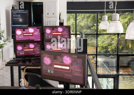 Multiple computer monitors in vacant office display warning messages indicating unauthorized access to company data. Empty workstations show hacked system alerts and compromised network security. Stock Photo
