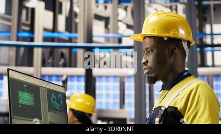 Smart factory employee typing on PC keyboard, testing automated systems, doing maintenance. Industry 4.0 plant staff member using computer to inspect equipment and repair bugs, camera B Stock Photo