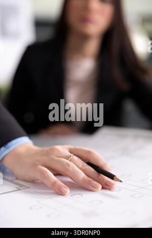 Close up of female hand holding pencil over printed design sheets, drafting blueprint details for construction project. Architect ready to draw elements on paper according to client measurements. Stock Photo