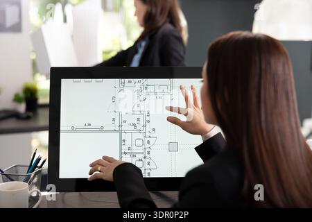 Female architect reviews detailed digital floor plan on touchscreen monitor. Professional designer evaluates layout measurements and prepares updated architectural documents for upcoming project. Stock Photo