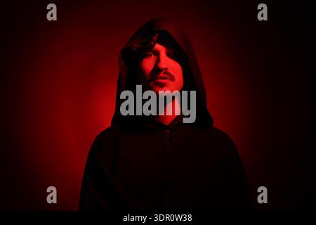 Man in hood on dark background with red light Stock Photo