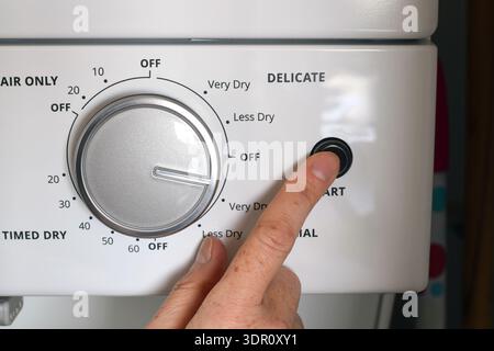 Closeup person finger pressing start button on household clothes dryer control panel. Home laundry routine concept of appliance operation, energy use, Stock Photo