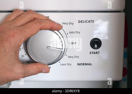 Closeup of person’s hand turning dial, adjusting settings on household clothes dryer control panel. Home laundry routine concept featuring appliance o Stock Photo