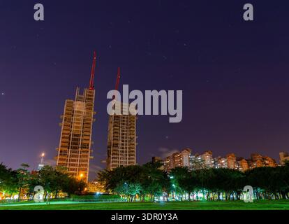 Two tall buildings under construction with red cranes stand tall against a starry night sky. Stock Photo